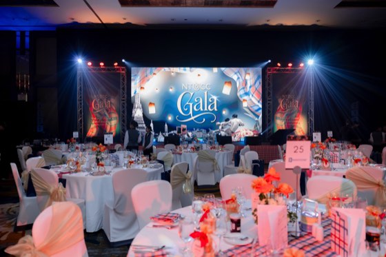 The gala ballroom set for dinner, the stage lit in red and blue